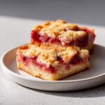 Two delicious squares of Strawberry Rhubarb Bars with a crumb topping, served on a white plate.
