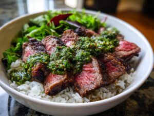 Close-up of a Wagyu beef steak chimichurri bowl featuring medium-rare sliced steak over white rice and greens.